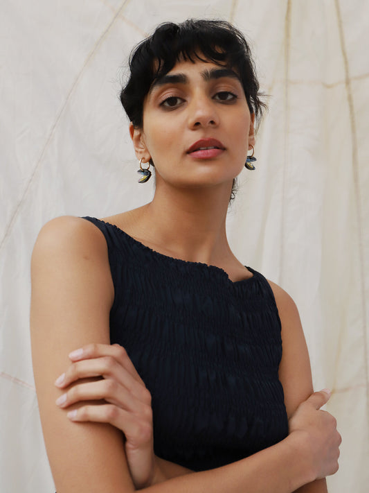 A lady in a black dress wearing a pair of mussel hoop earrings.
