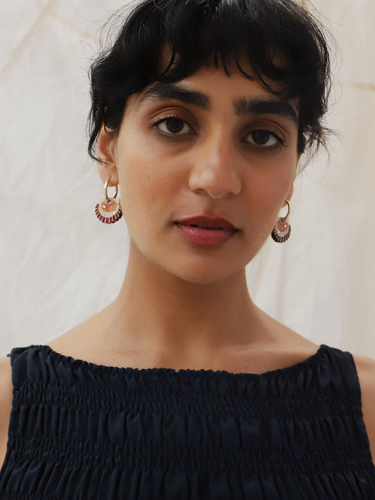A lady wearing a pair of scallop shell hoop earrings with pink, gold, and white colors and crystal details.