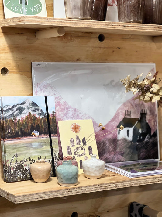 A wooden shelf decorated with a picture of a house and small vases.
