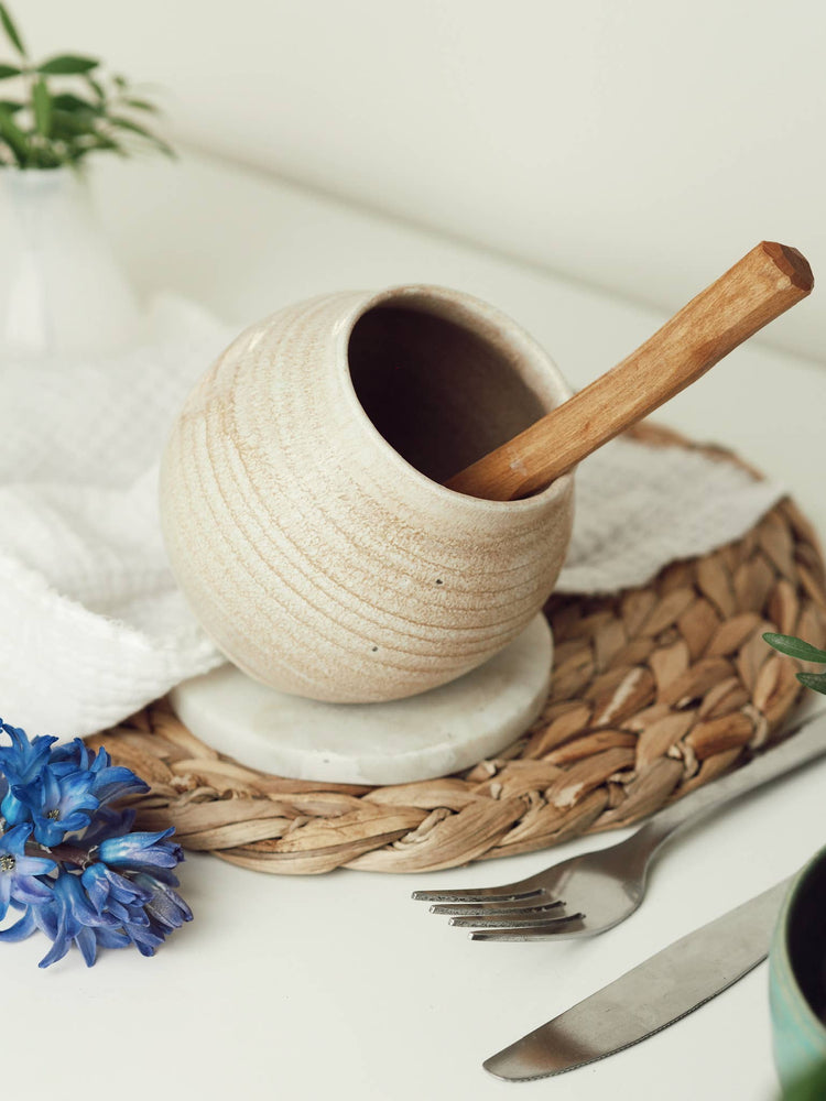 A handcrafted ceramic salt pig with a spoon inside it, sitting on a stone mat.