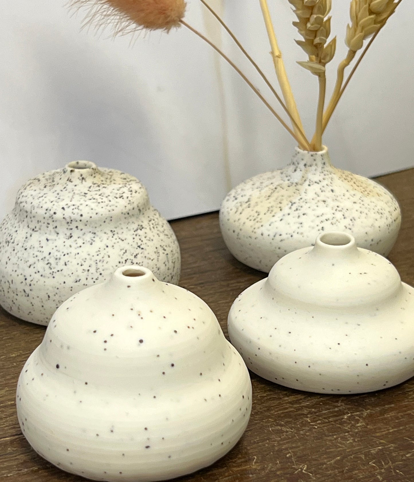Four white ceramic vases with speckled texture on a wooden surface.
