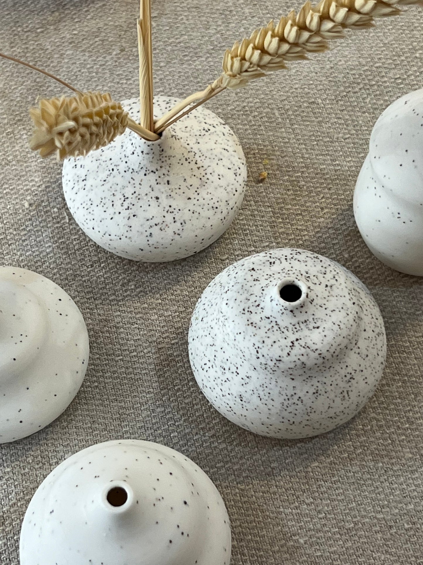 Speckled ceramic pots on a textured surface with wheat stalks.